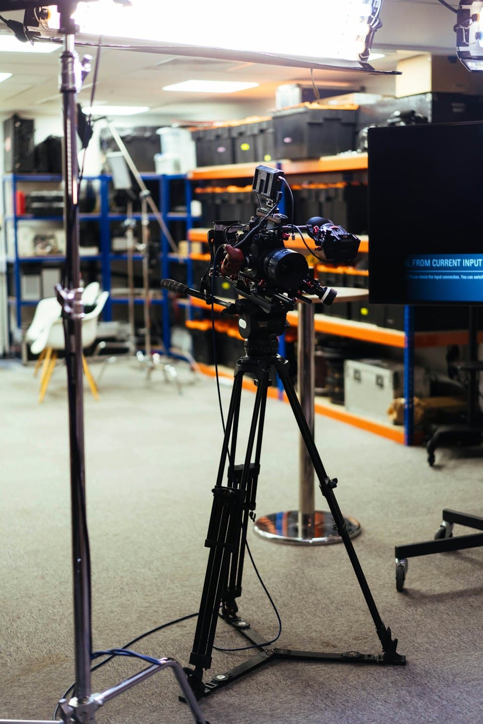 Professionele videocamera op statief in een magazijn vol apparatuur.